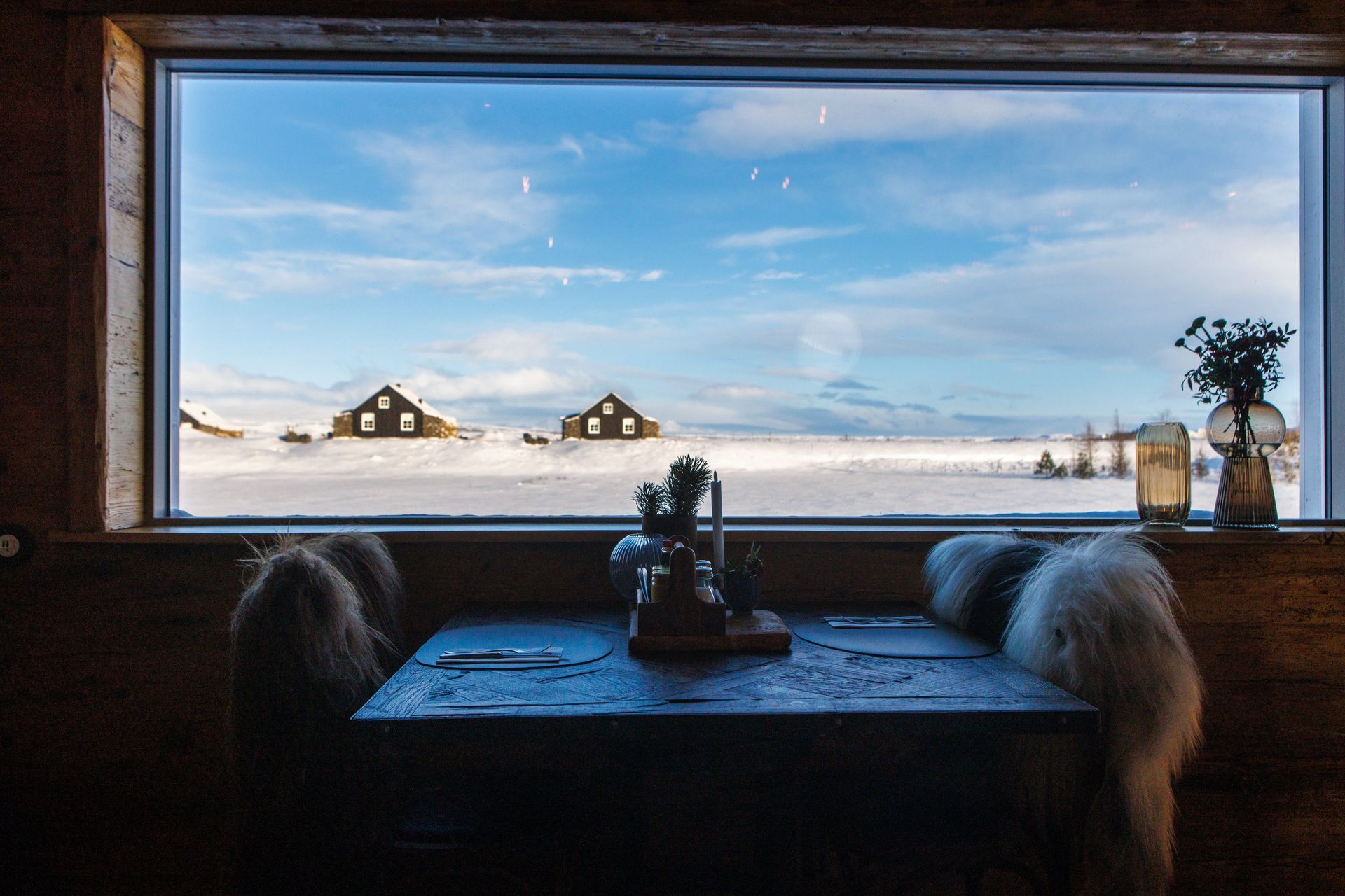 A table and chairs in front of a window with a view of a snowy field.