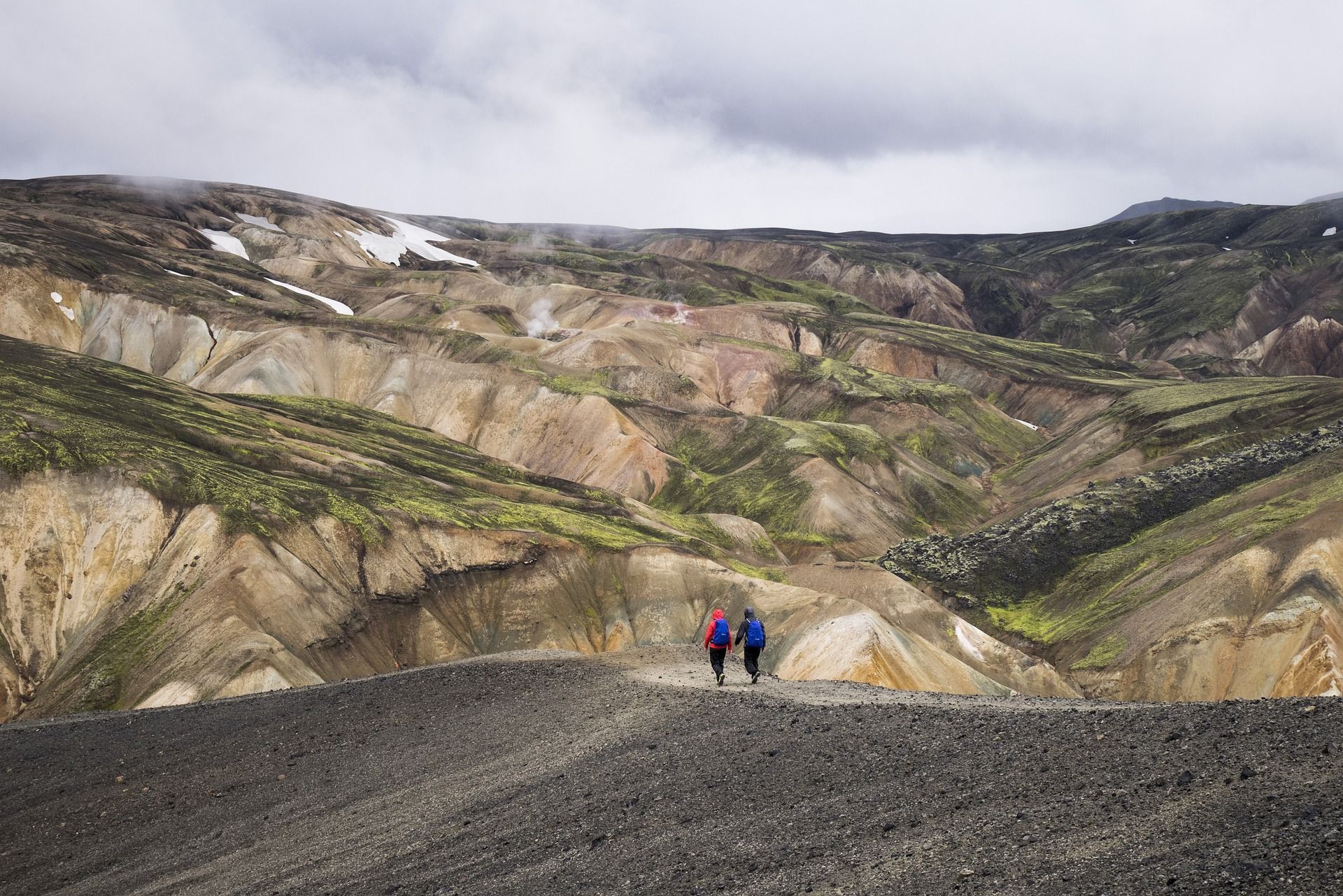 Two people are walking down a dirt road in the mountains.
