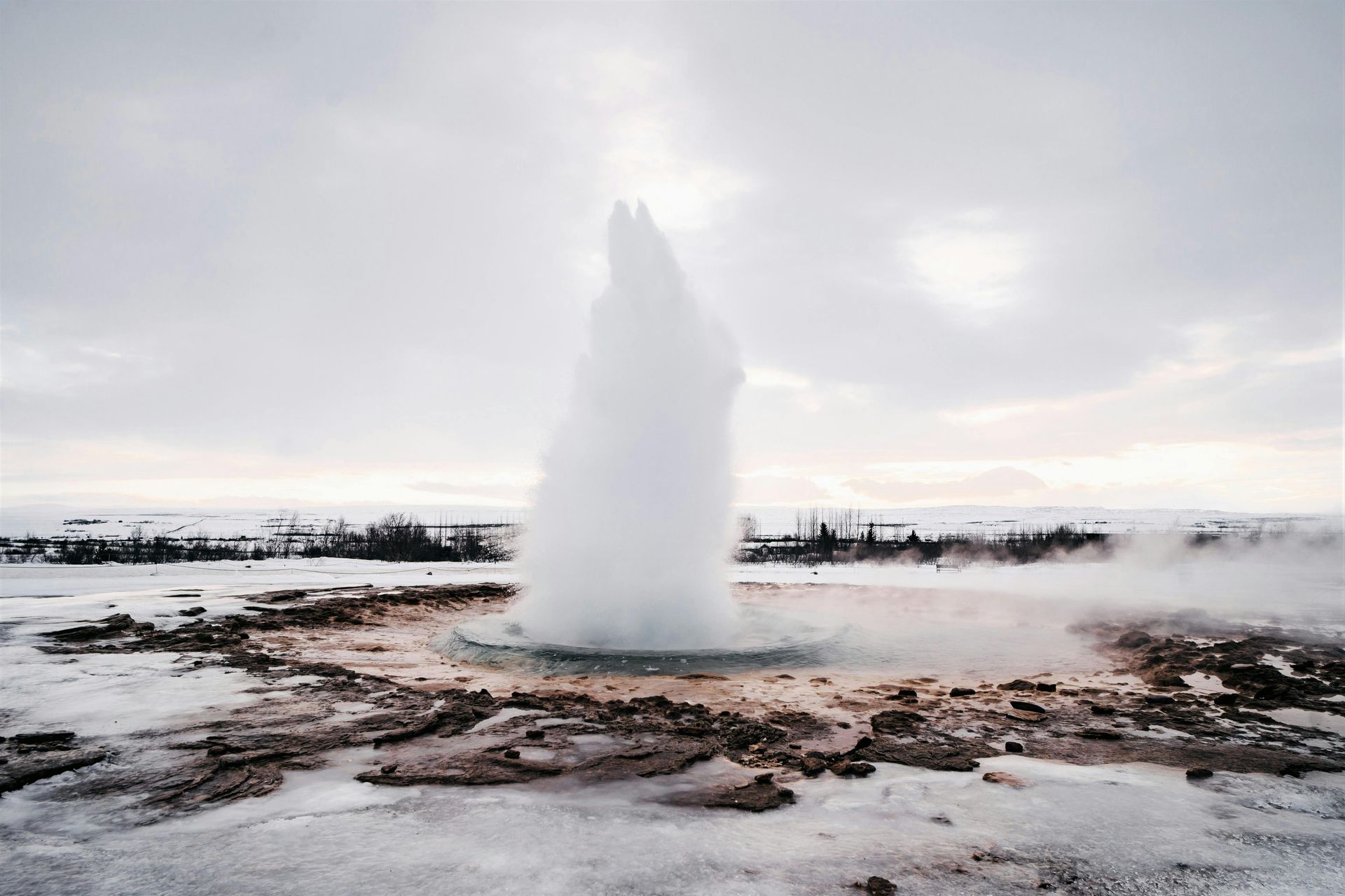 A geyser is erupting in the middle of a snowy field.