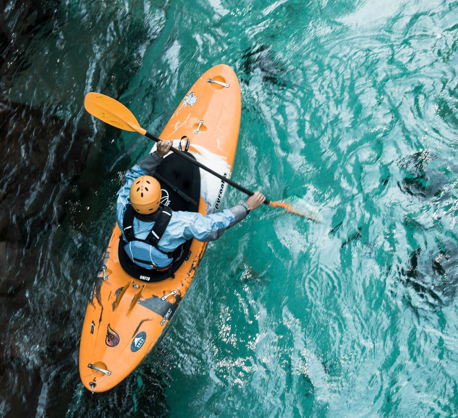A person in an orange kayak is paddling down a river.
