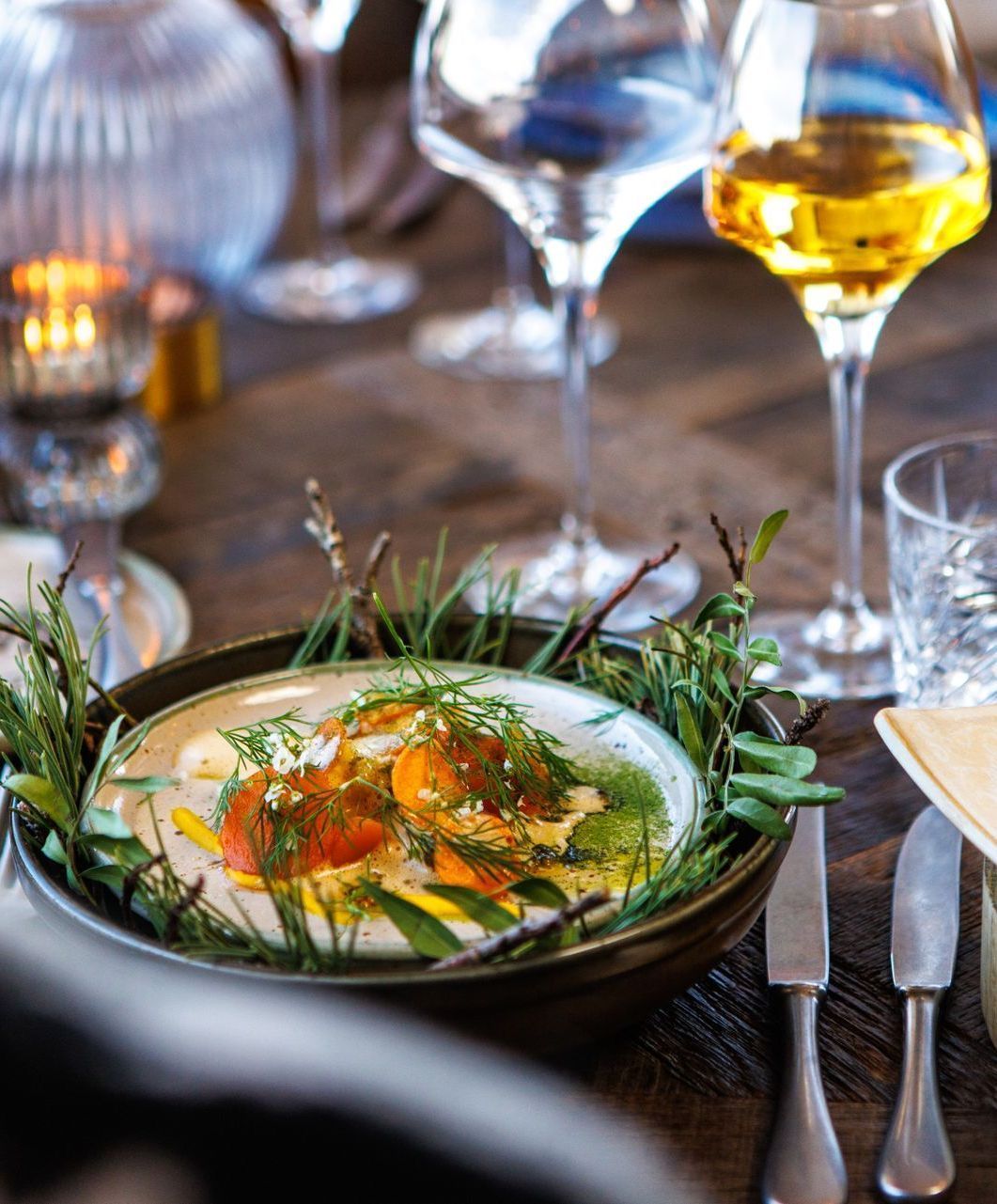 A bowl of food is sitting on a wooden table next to wine glasses.