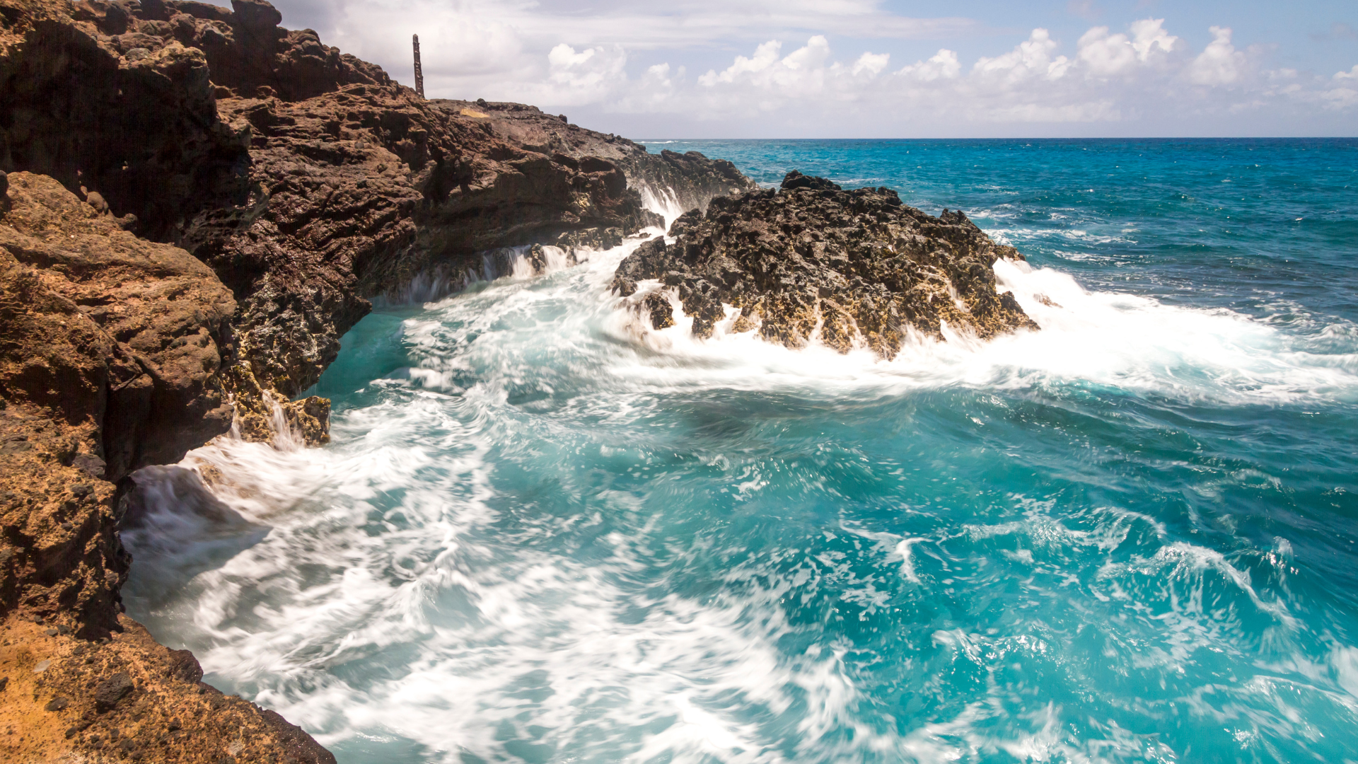 A person is standing on a rocky cliff overlooking the ocean.