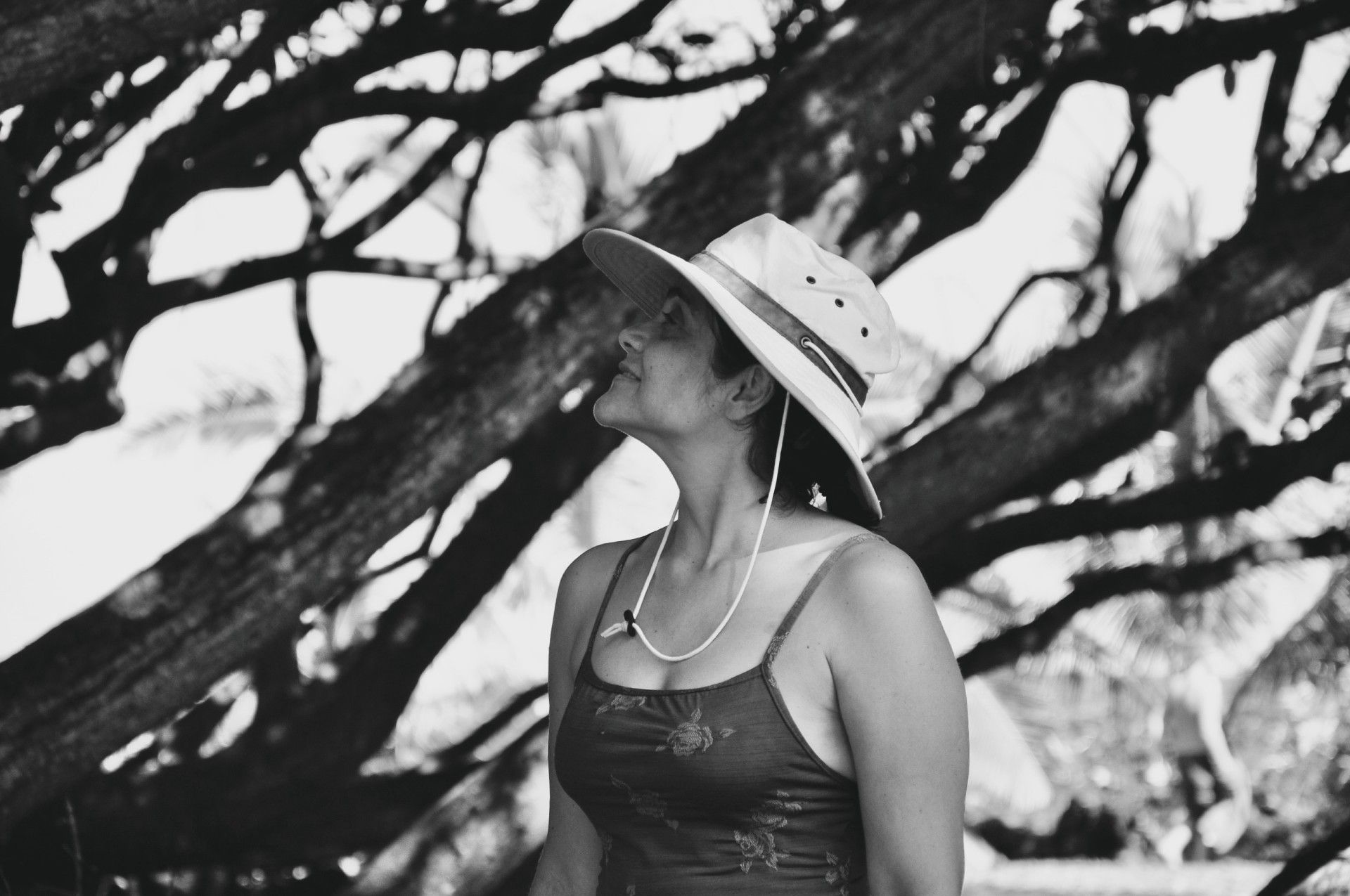 A woman wearing a hat and a necklace is standing under a tree.