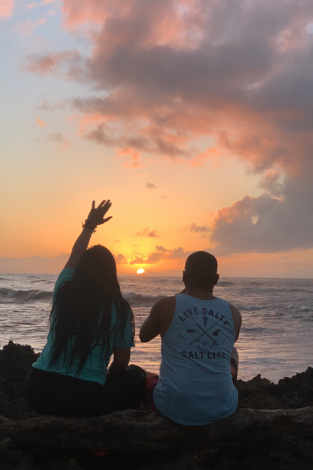 Two people waving at the sunset on the ocean