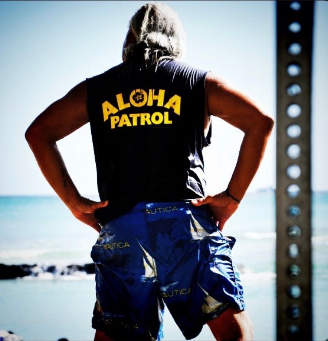 A man wearing an aloha patrol shirt stands on the beach