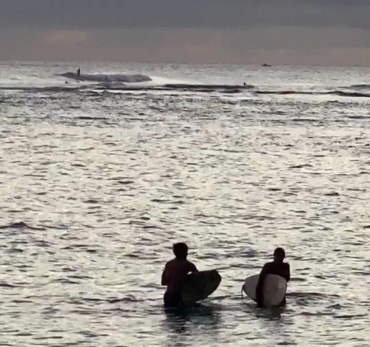 Two surfers are standing in the ocean holding surfboards.