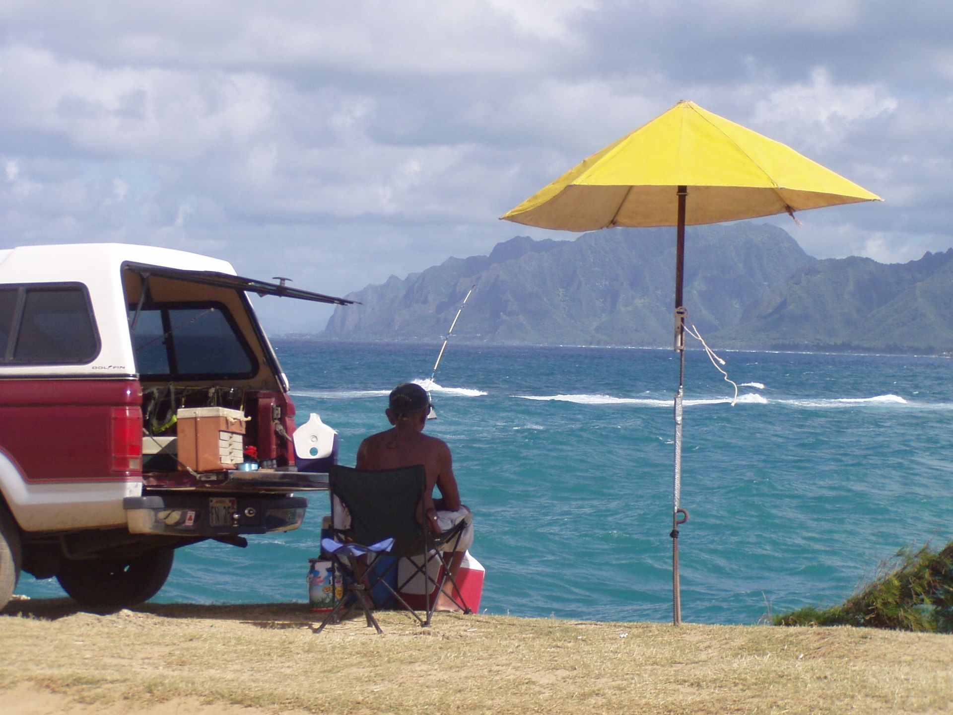 A man sits under a yellow umbrella near the ocean