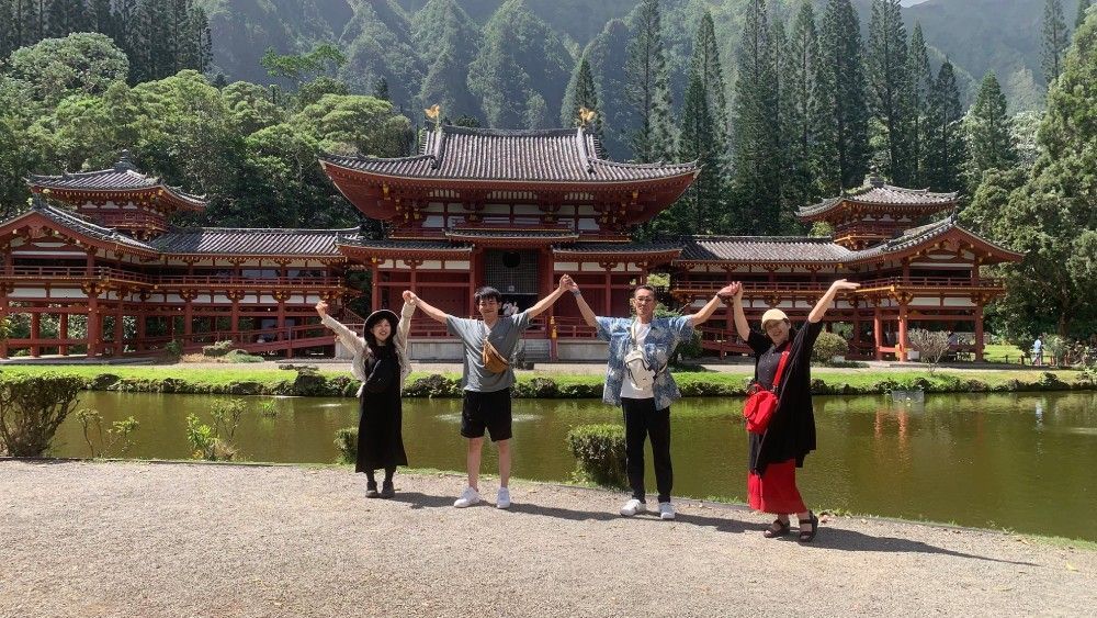 Two people watching a sunset over the ocean as a wave crashes, sending water spray into the air.