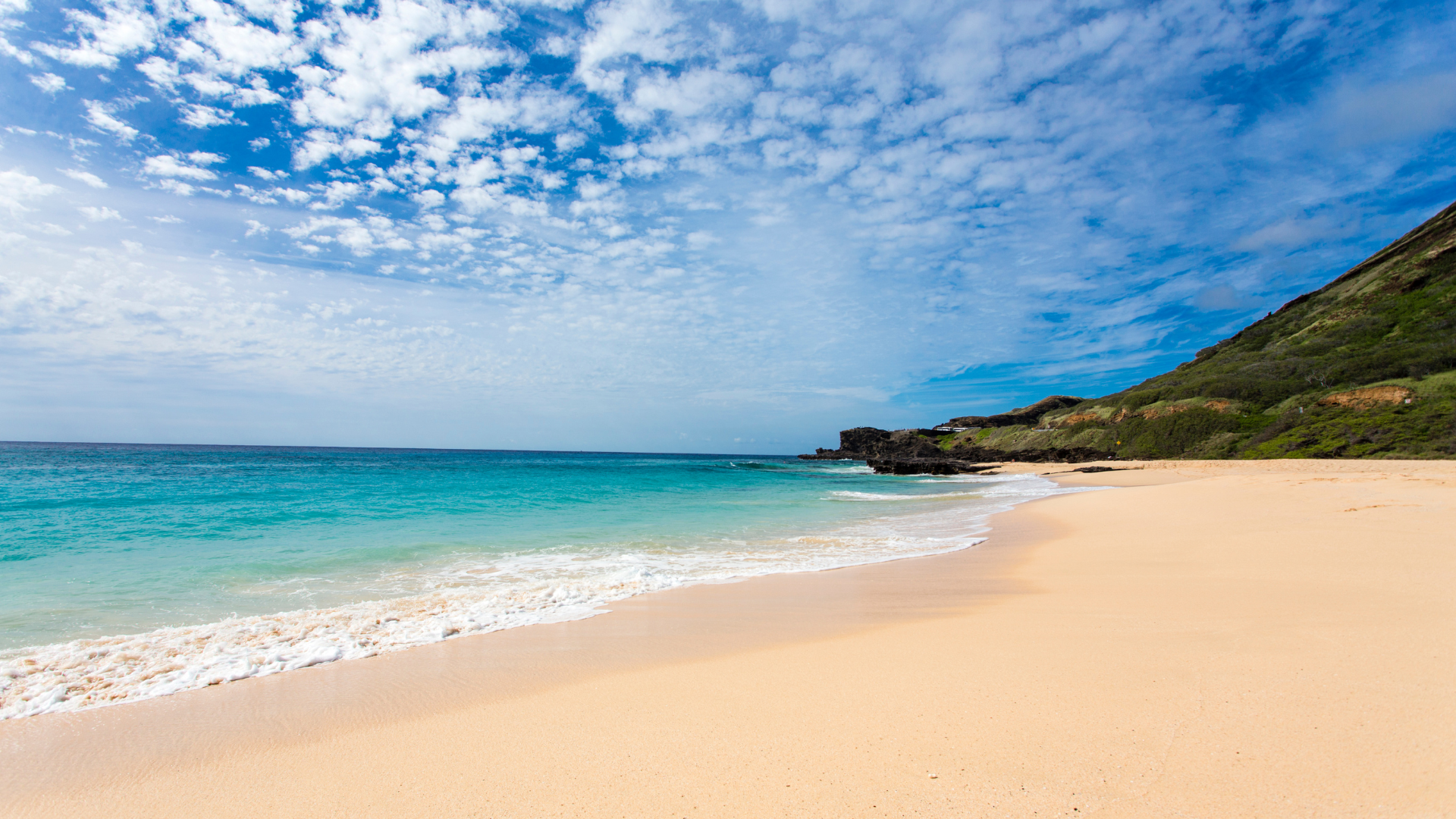 There is a beach with a mountain in the background and a blue ocean.