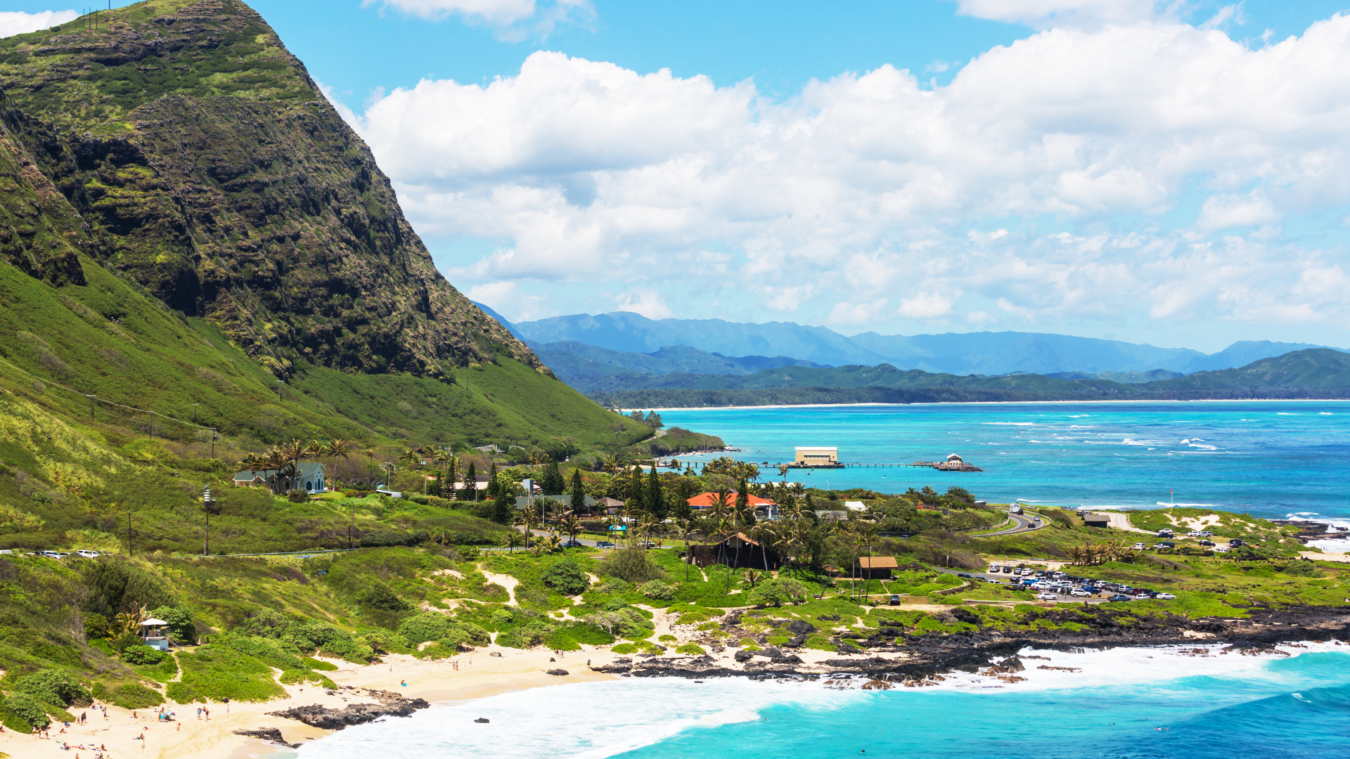 A beach with a mountain in the background and a body of water in the foreground.