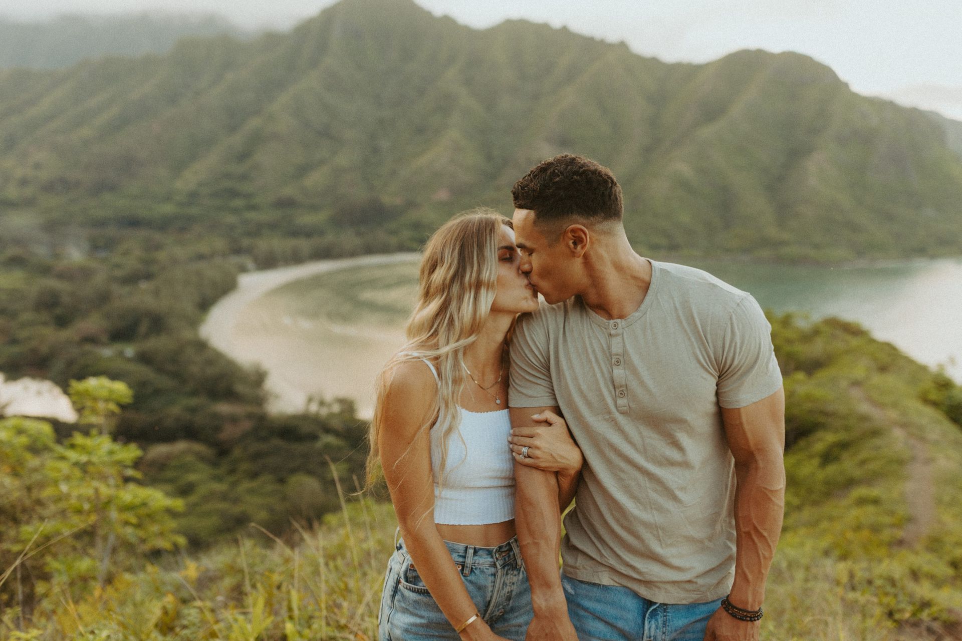 A man and a woman are kissing on top of a hill.