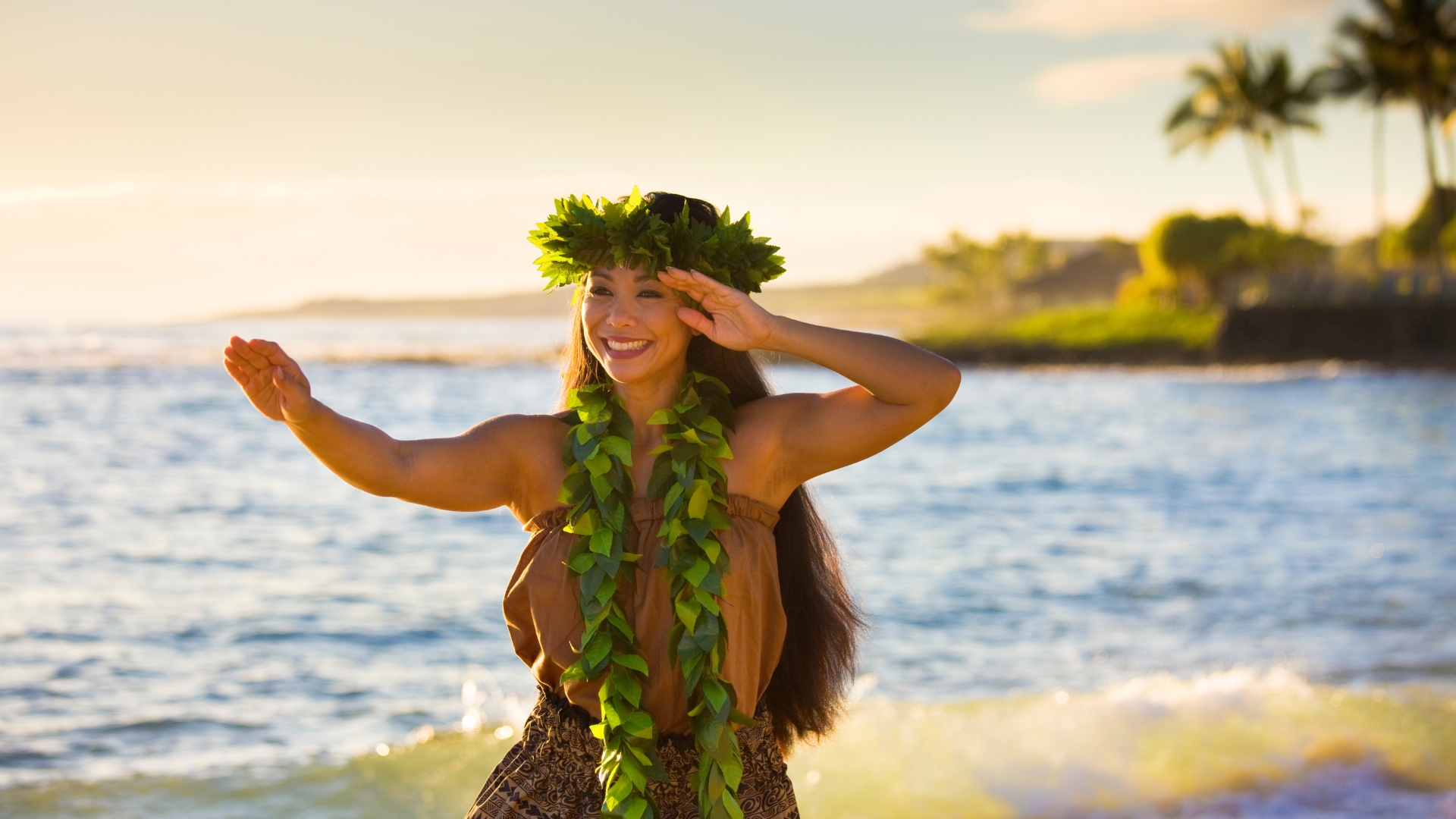 A woman wearing a lei is dancing on the beach.