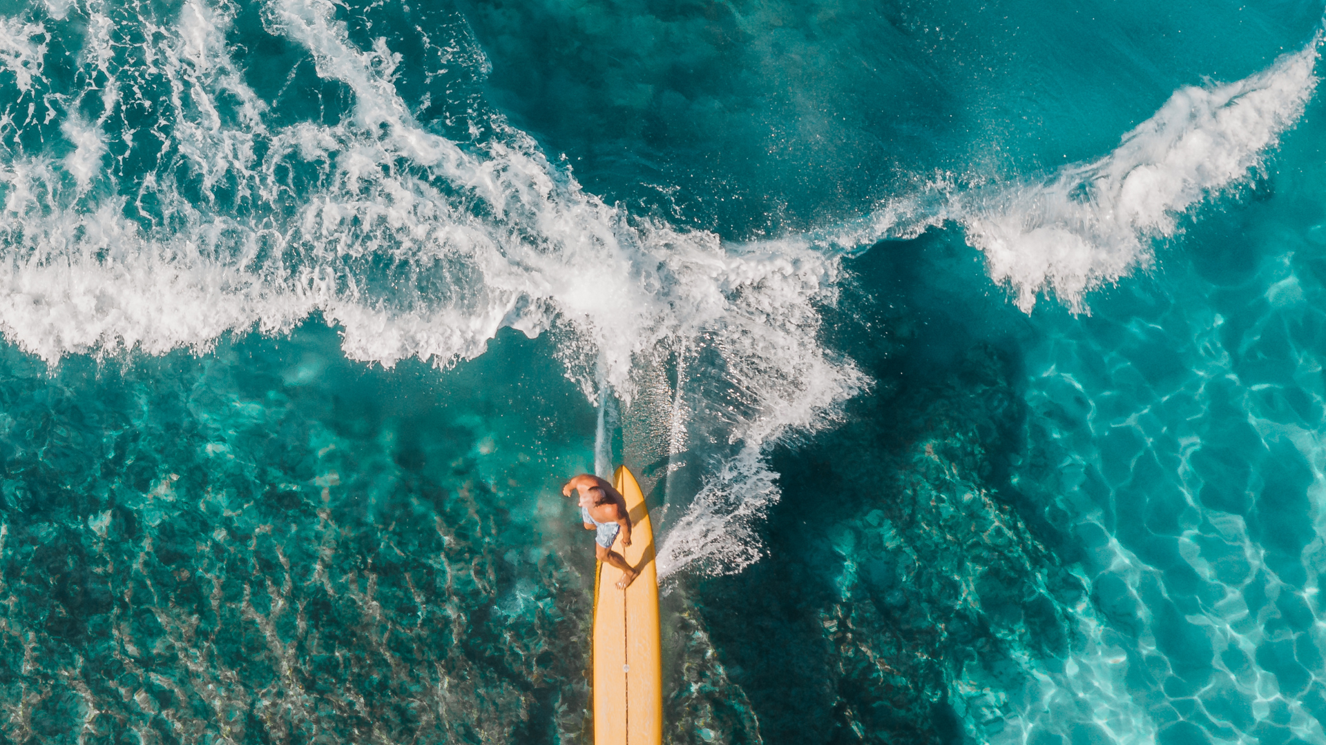 An aerial view of a person riding a wave on a surfboard in the ocean.