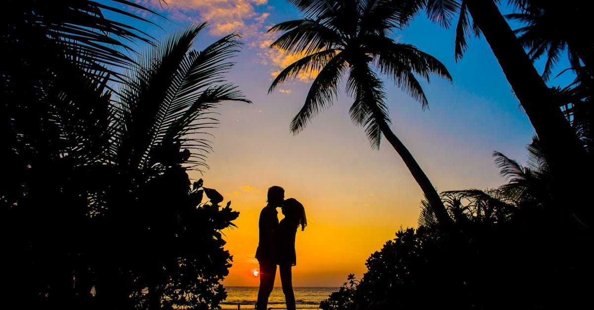 A man and a woman are kissing on a beach at sunset.