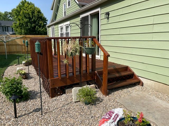 A wooden deck with stairs is in front of a green house.