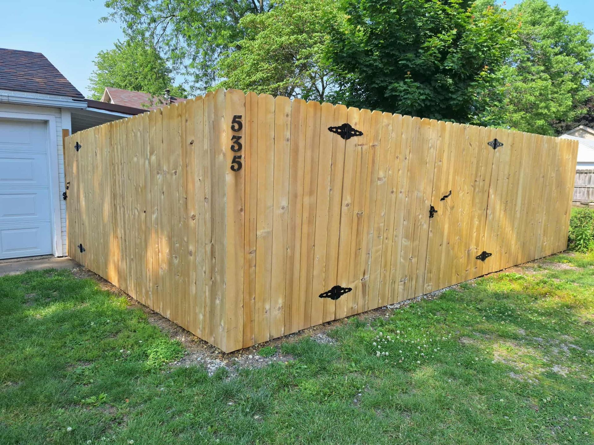 A wooden fence is sitting in the middle of a lush green yard next to a garage.