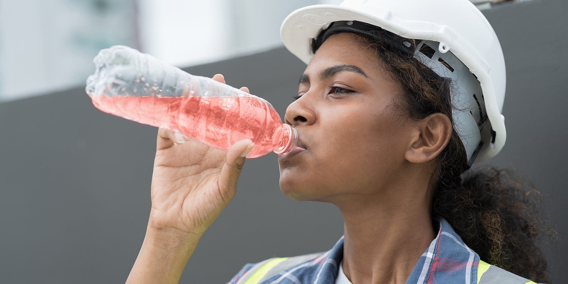 A woman wearing a hard hat is staying hydrated by drinking Ready/Go® Hydration. 