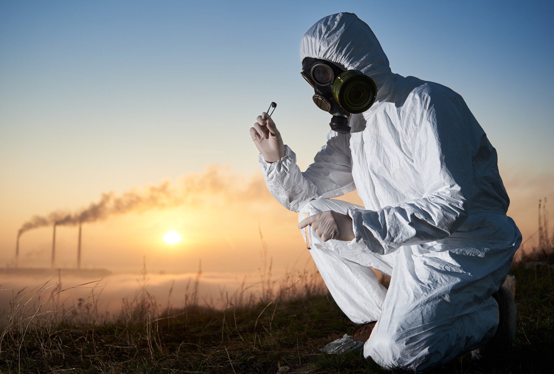 A man wearing a hazmat suit and gas mask is holding a sample with tweezers. 