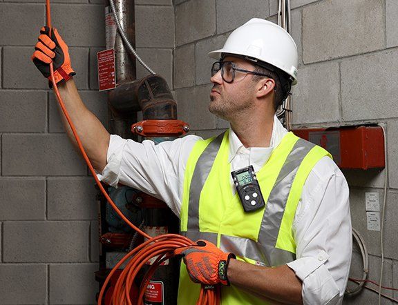 A man is running wires in a warehouse and has a Nextteq® NXM Series Multi Gas Detector clipped to his vest.