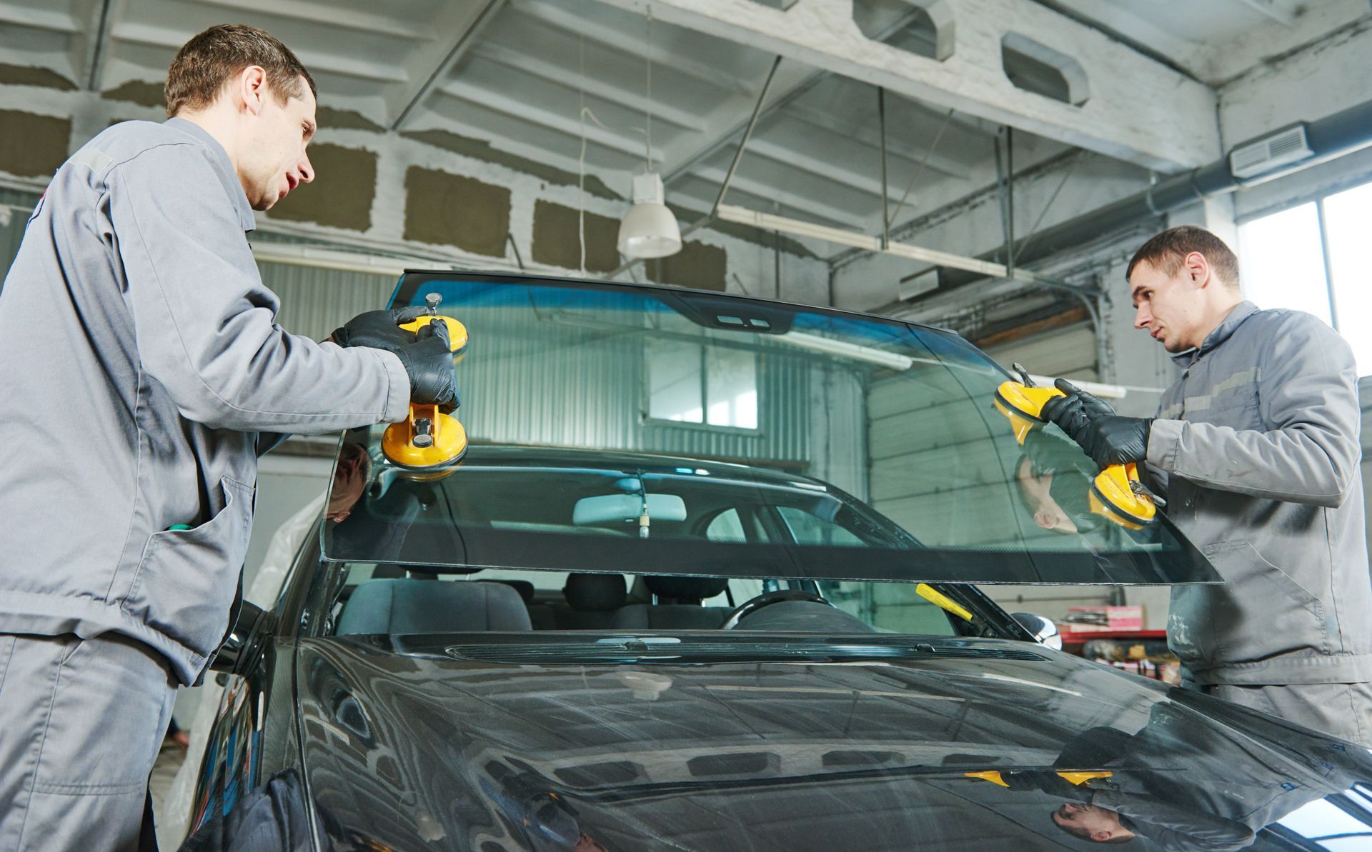 Technicians installing a new windshield on a car using suction tools.