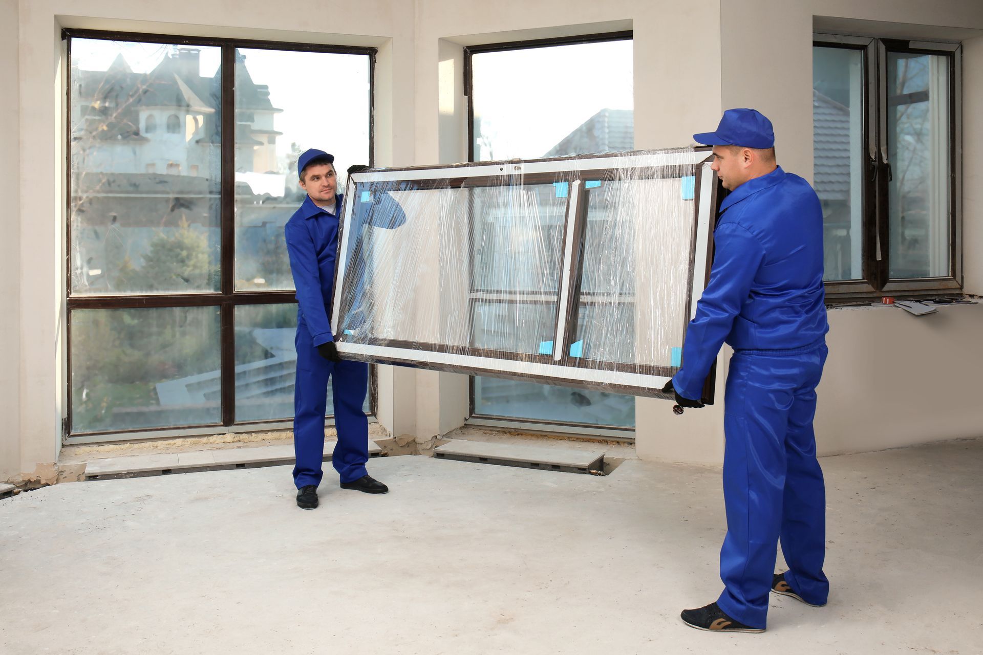 Workers installing a large window frame in a building under renovation.