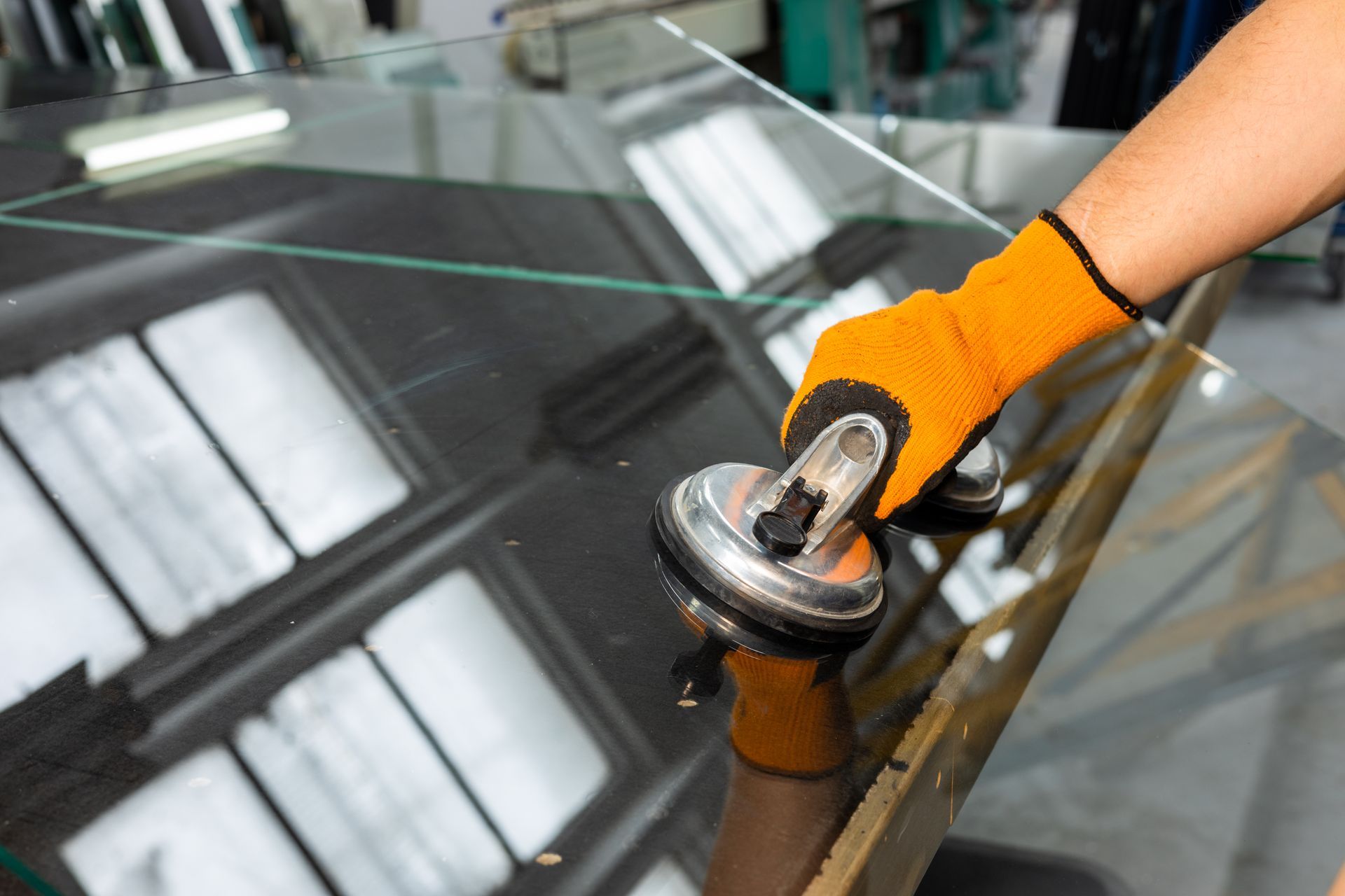 A worker using a suction lifter to handle a large glass pane during installation.