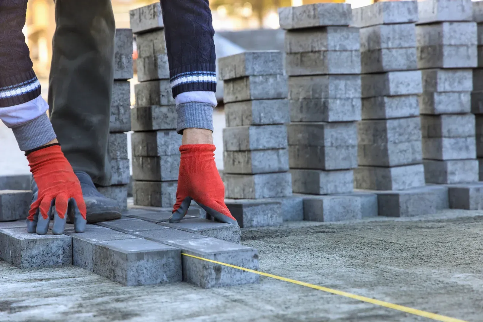 A person wearing red gloves is laying bricks on a sidewalk.