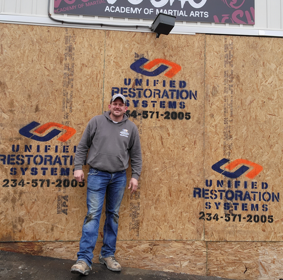 Owner Jason in front of a boarded up hole in a brick wall - Unified Restoration Systems