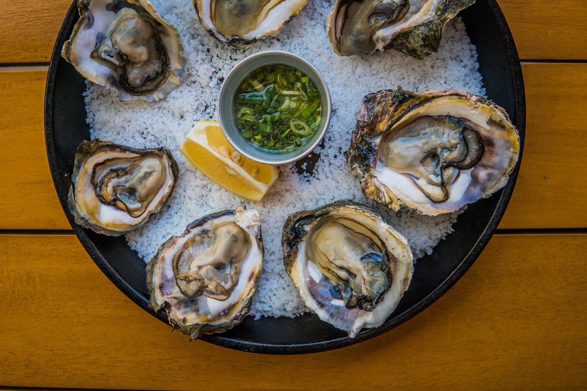 A plate of oysters with sauce and a slice of lemon on a wooden table.