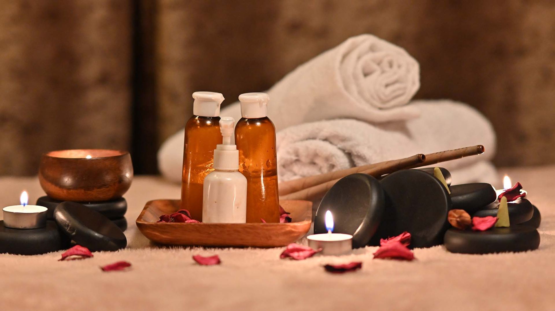 There are bottles of oil , candles , towels and rocks on the table.