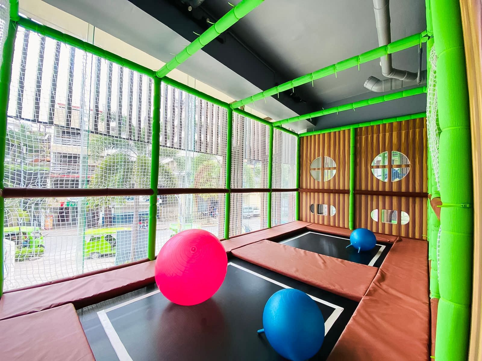 Indoor playground with trampolines, large bouncy balls, and wooden panel walls.
