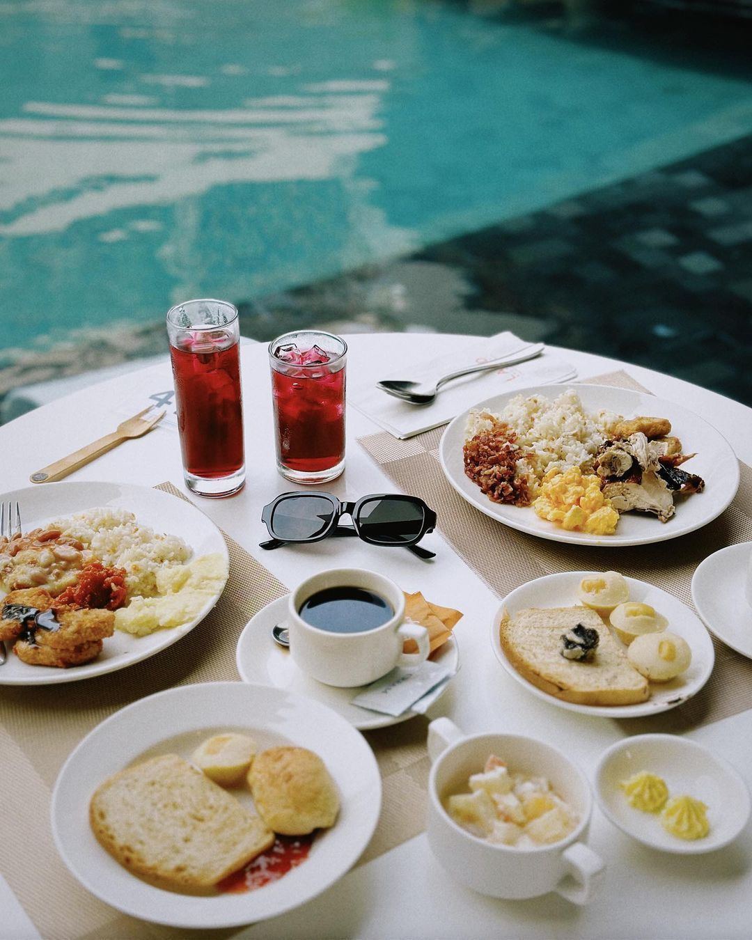 A table with plates of food and drinks next to Hue's pool by La-ud