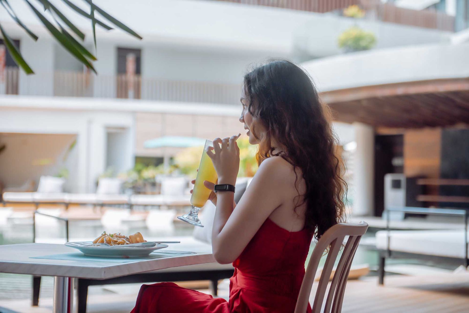 A woman in a red dress is sitting at a table drinking orange juice at top restaurants in Boracay