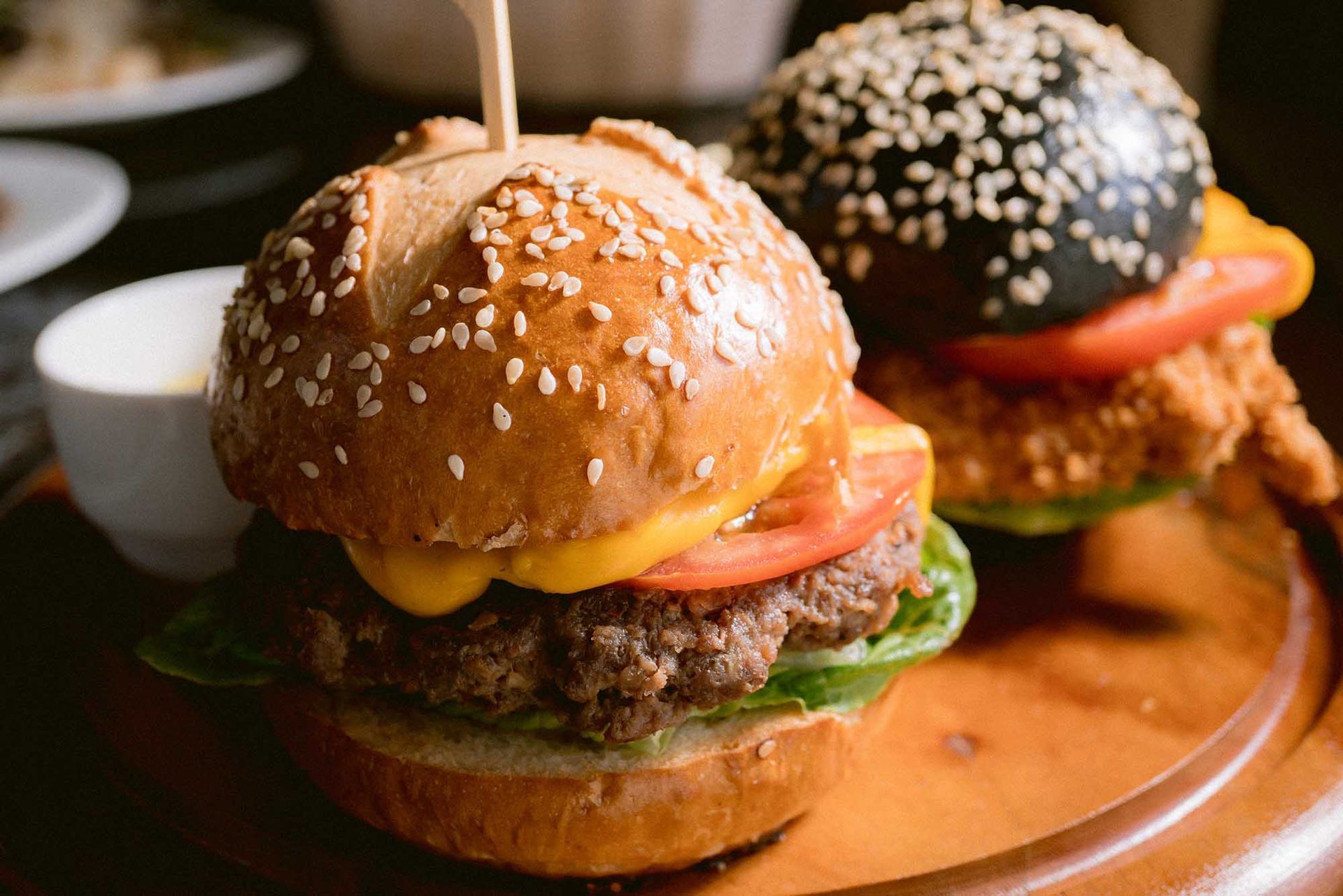Two hamburgers are sitting on a wooden cutting board.