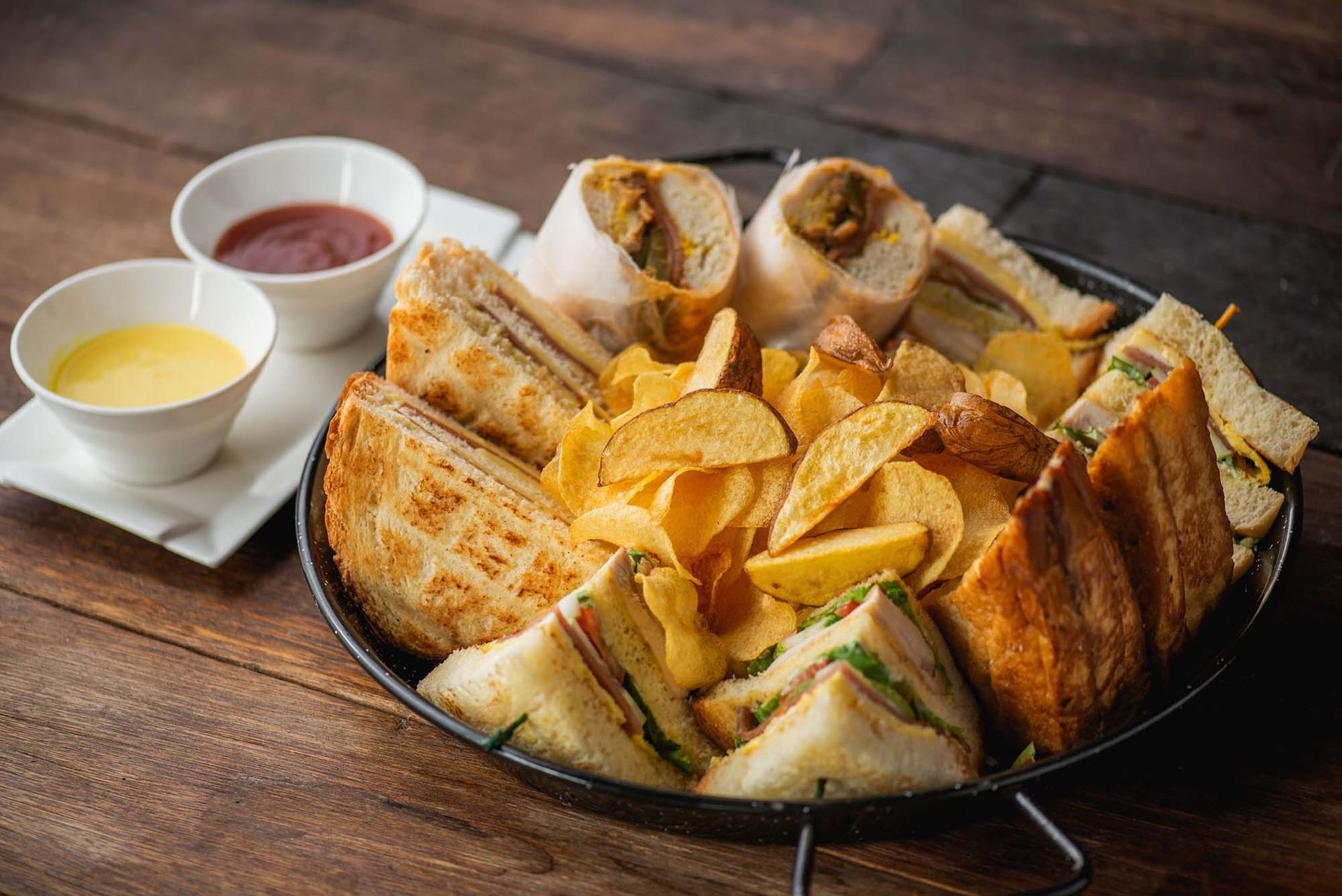 A pan filled with sandwiches and chips on a wooden table.