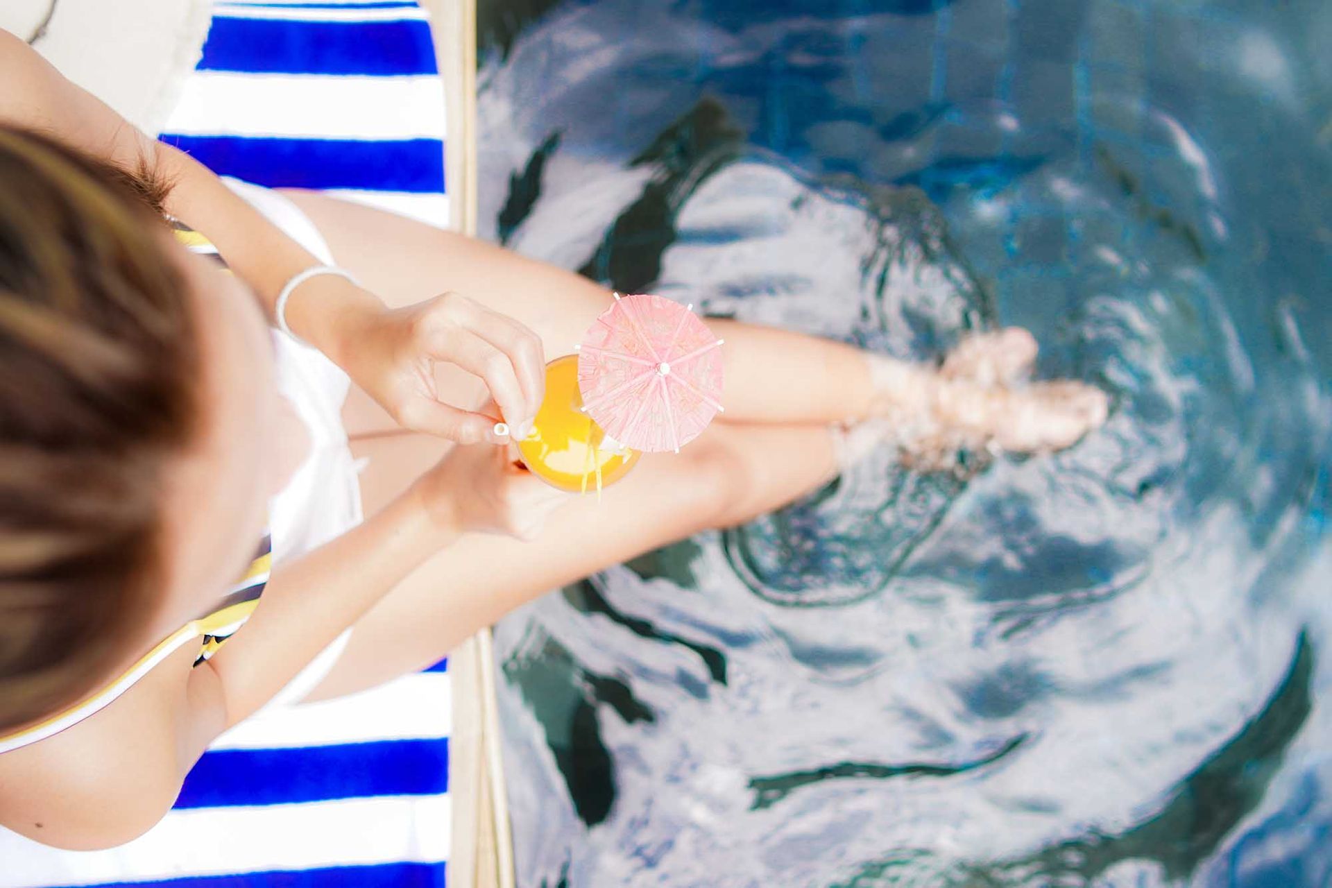 A woman in a bikini is sitting on a striped towel in a swimming pool.