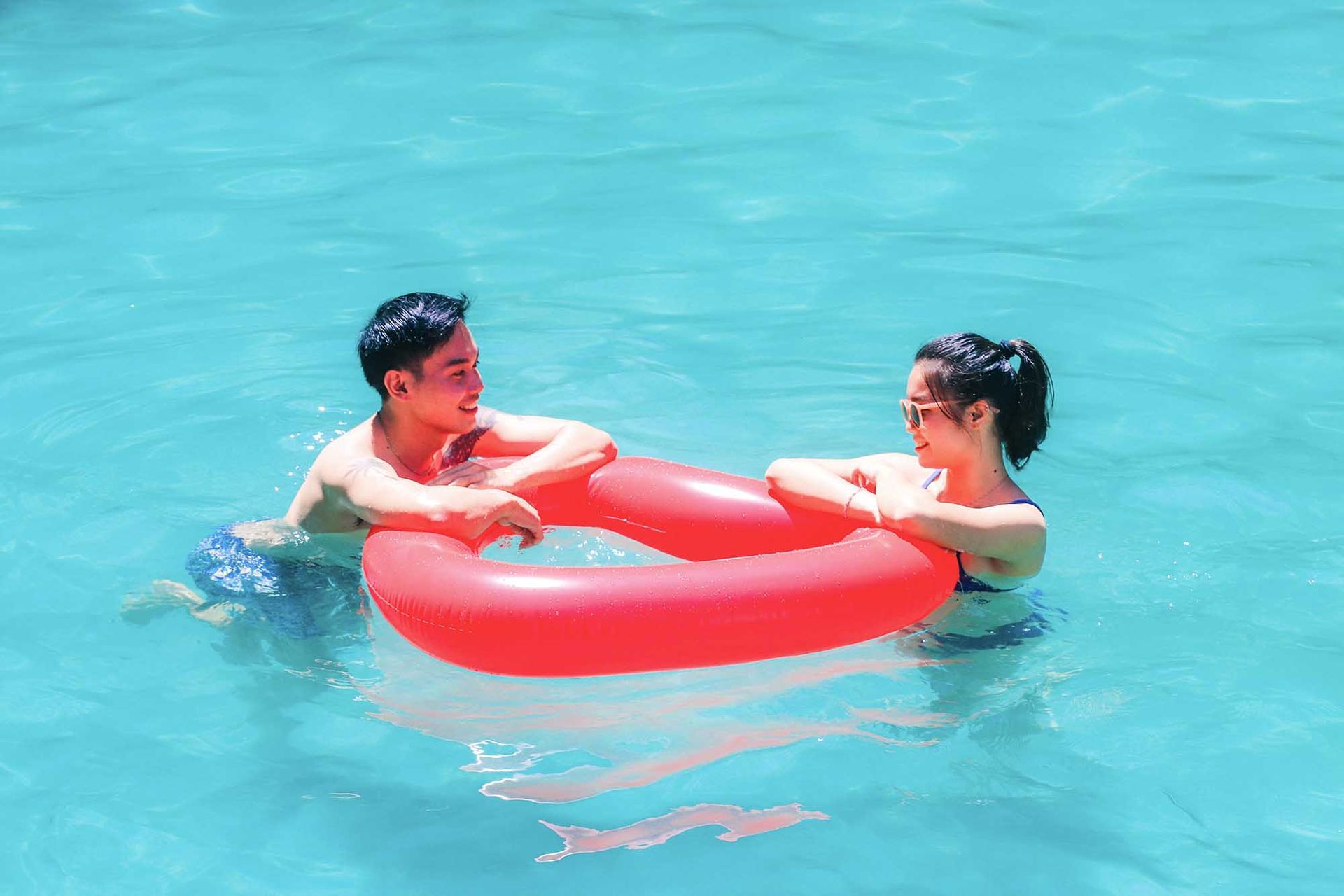 Two people in a pool, holding a red inflatable ring and smiling.