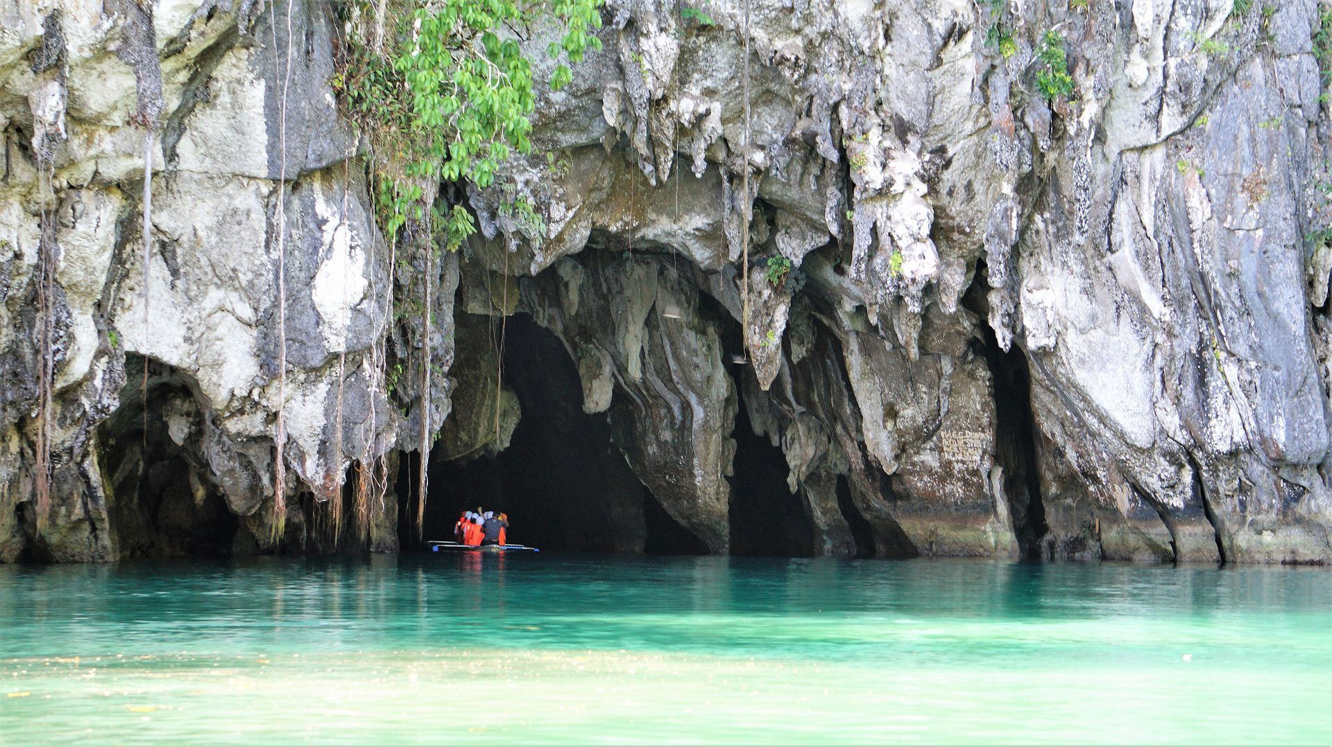 A group of people are in a boat in front an underground cave in Palawan