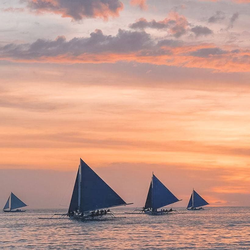Three sailboats are sailing in the ocean at sunset in Boracay