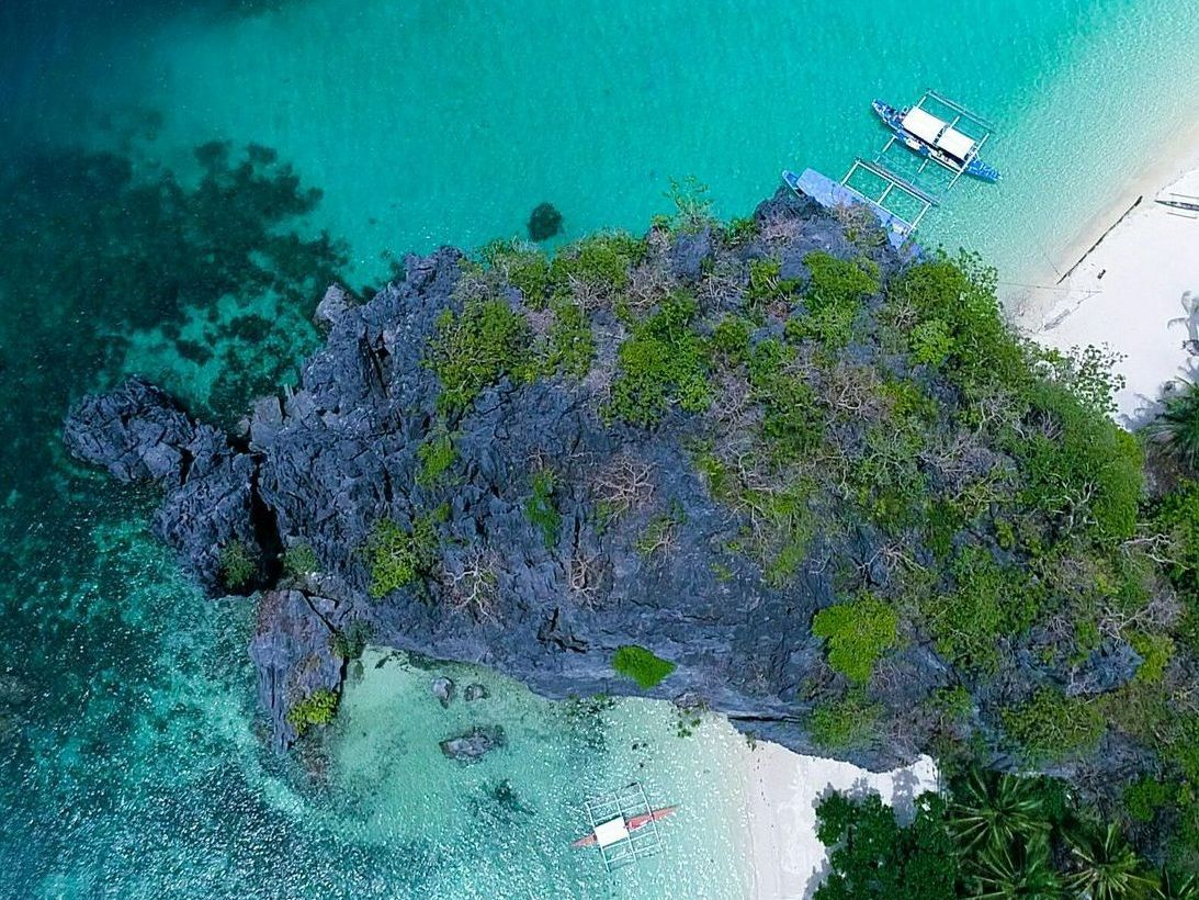 Aerial view of pristine beach cove near Hue Hotel - Puerto Princesa with traditional bancas and limestone cliffs