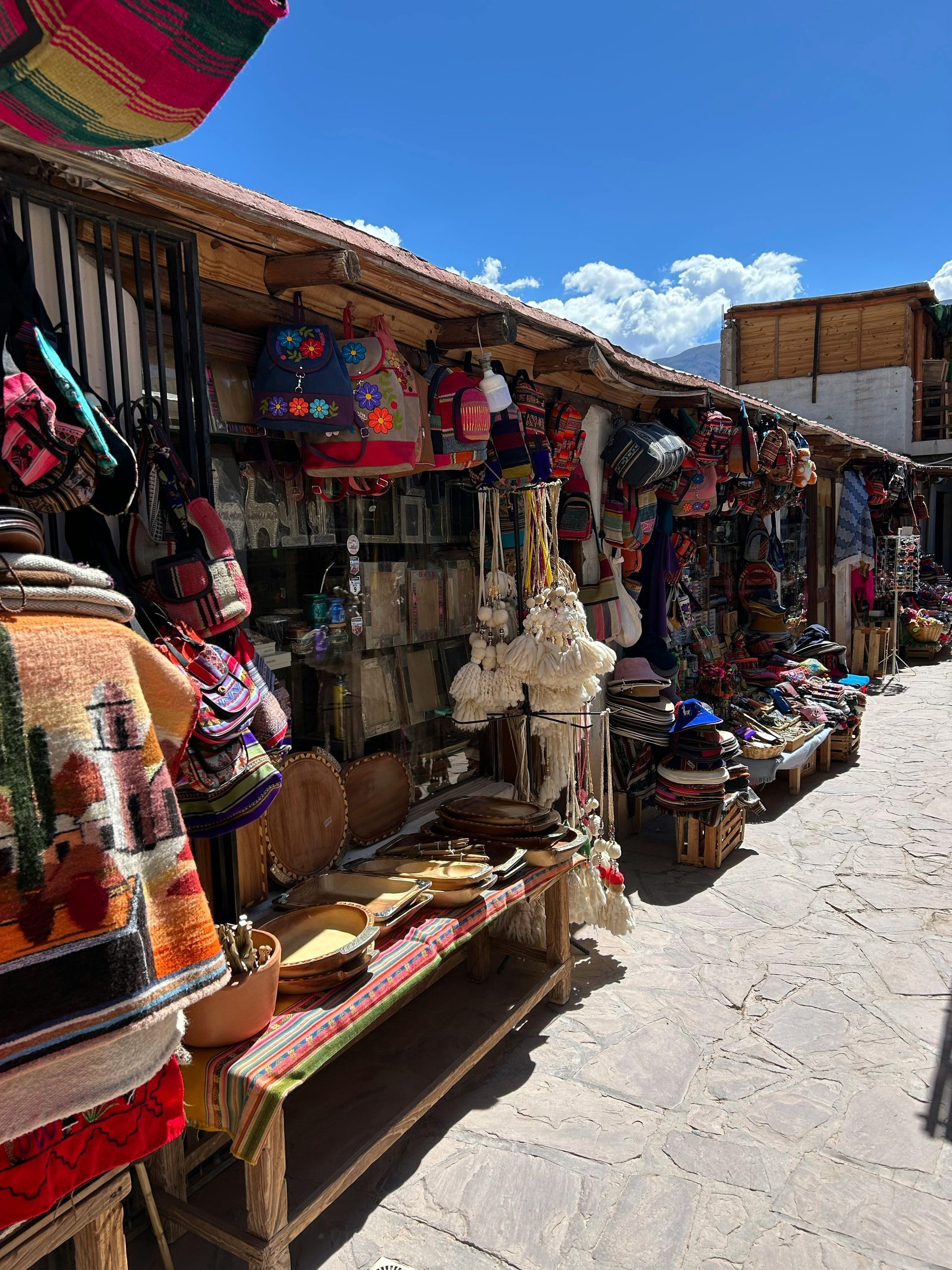 Row of vendor stalls selling colorful handicrafts under a blue sky.