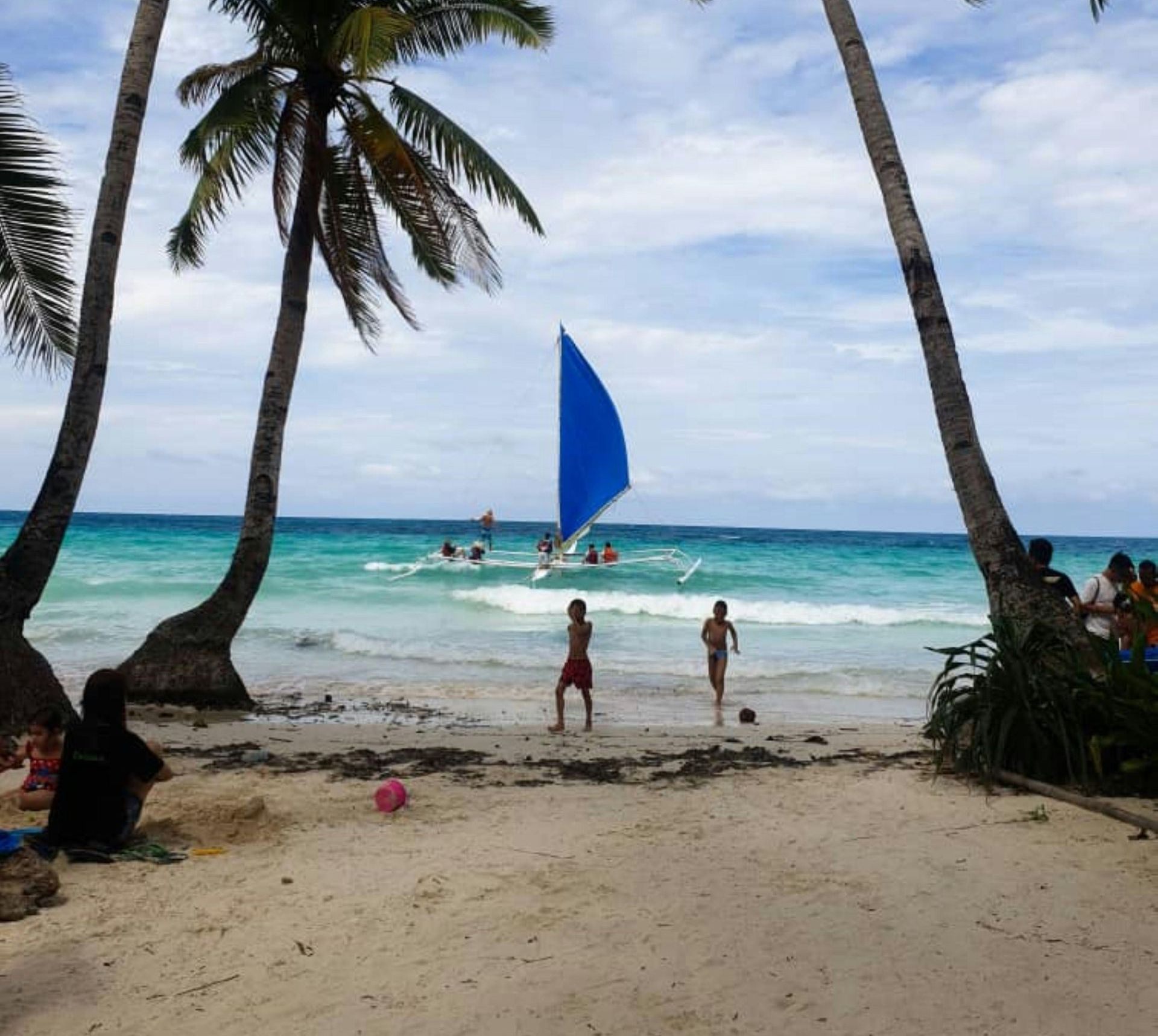 People on a beach with a blue sailboat in the background