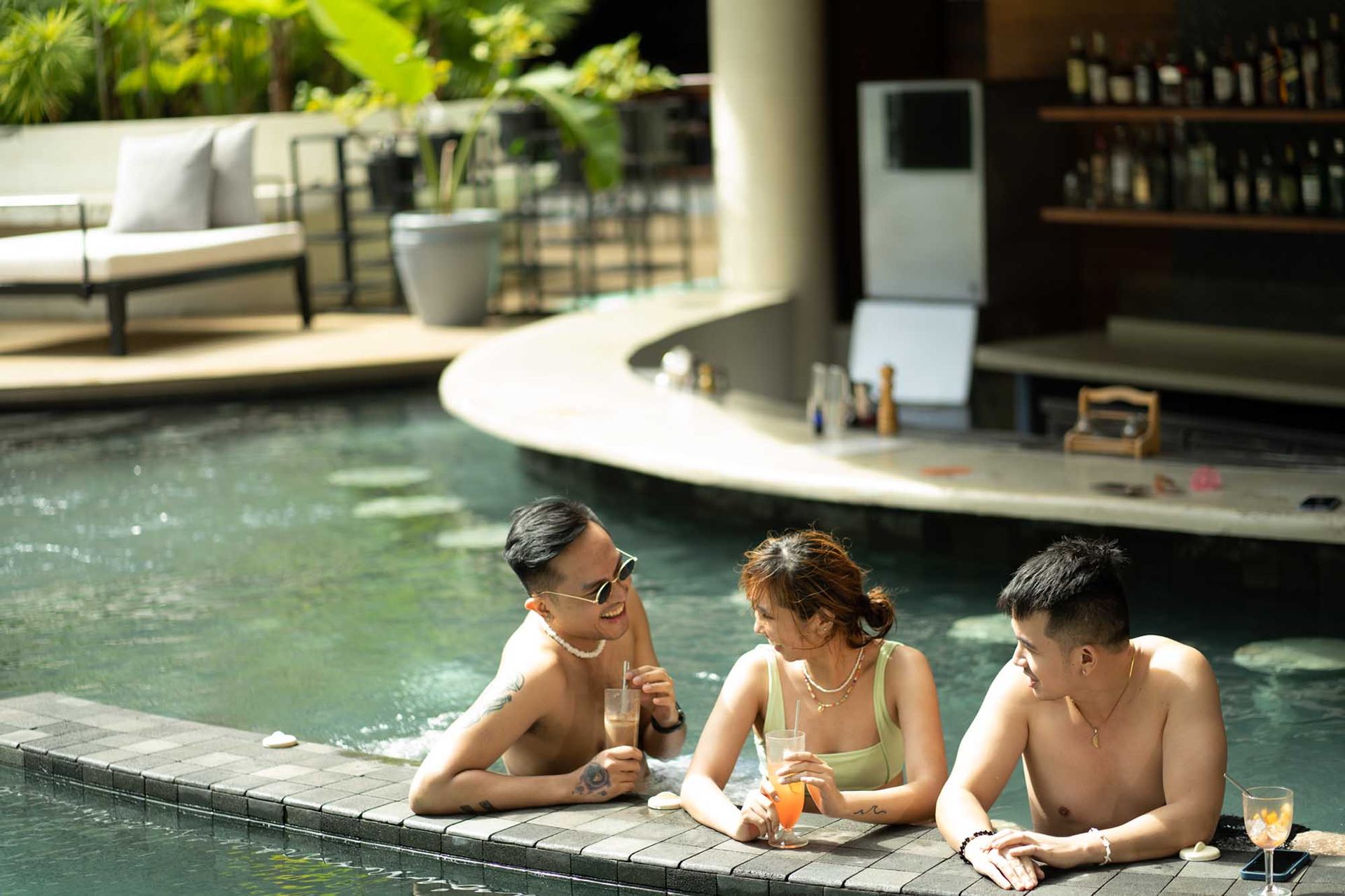 Three people are sitting on the edge of a flamingo pool bar.