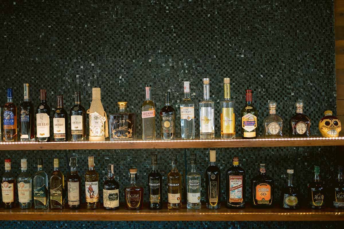 Two wooden shelves against a dark speckled wall, lined with a variety of glass liquor bottles.