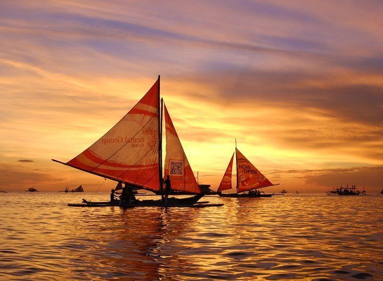 Sailboats on water silhouetted against a golden sunset sky.