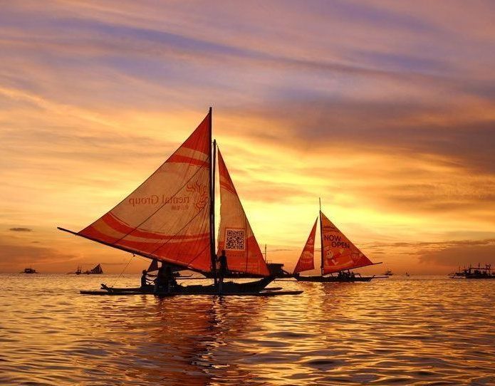 Traditional paraw sailing boats against golden sunset at White Beach Boracay