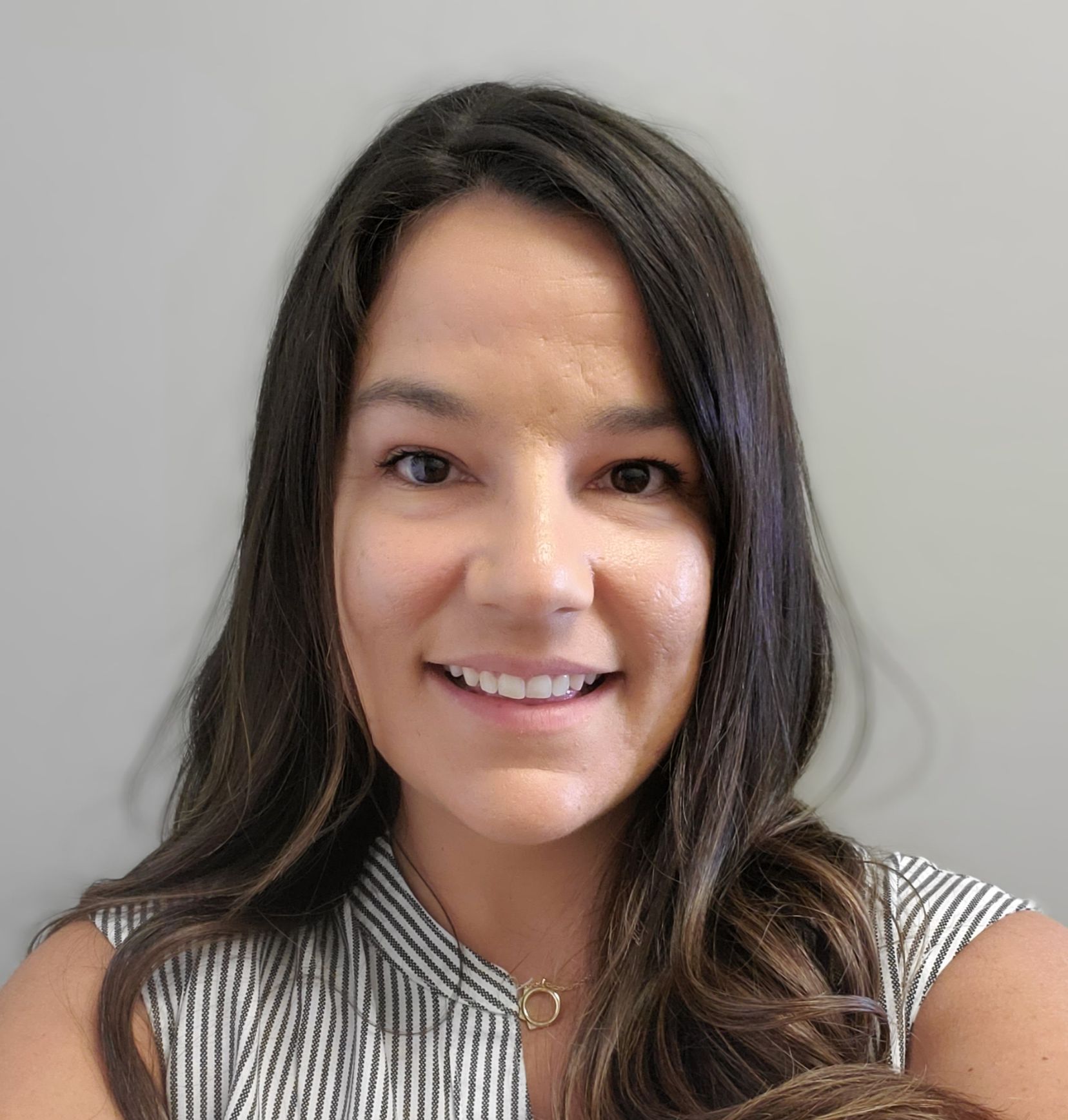 Woman smiling, wearing a striped blouse, long dark hair, against a gray background.