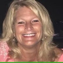 Blonde woman smiling, wearing a pink top.