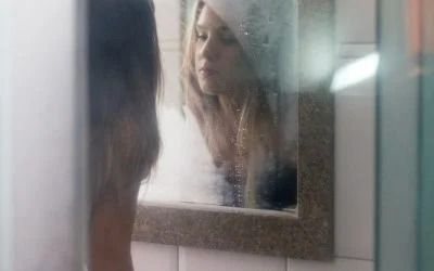 A woman is looking at her reflection in a bathroom mirror.