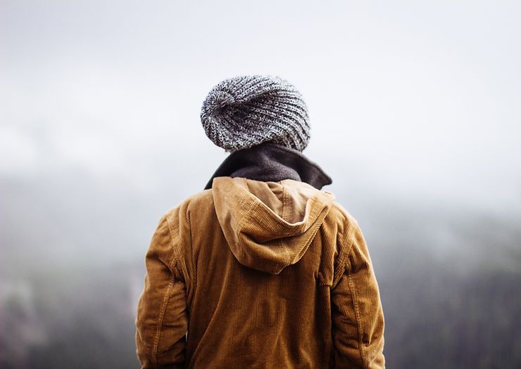 A man wearing a hooded jacket and a knitted hat is standing on top of a hill.